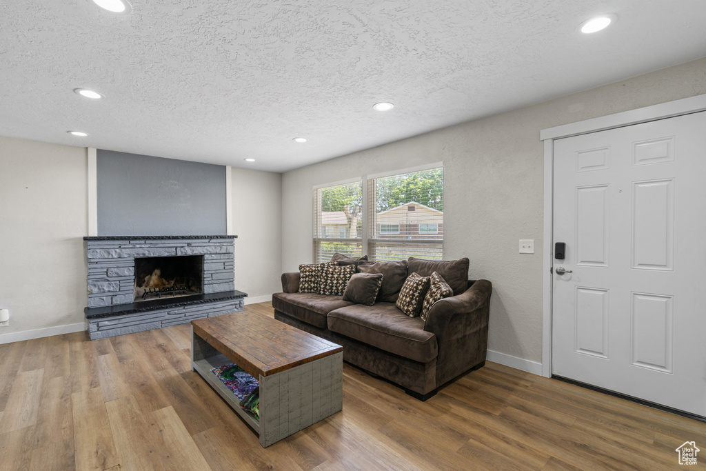 Living area featuring a textured ceiling, wood finished floors, recessed lighting, and a stone fireplace