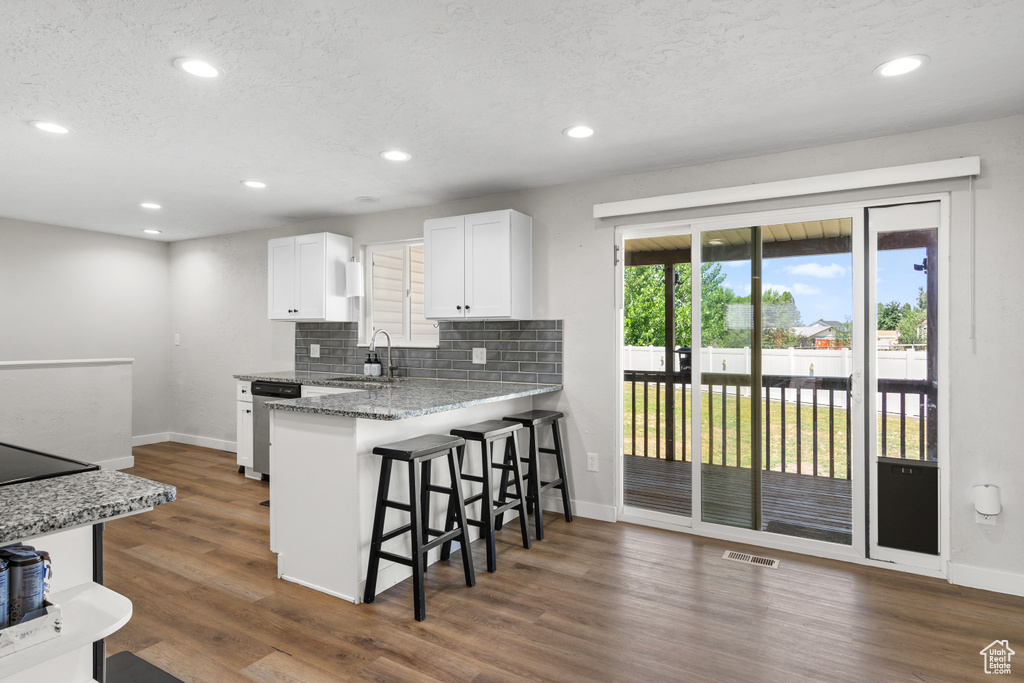Kitchen featuring a breakfast bar area, white cabinets, tasteful backsplash, recessed lighting, and dark wood-type flooring