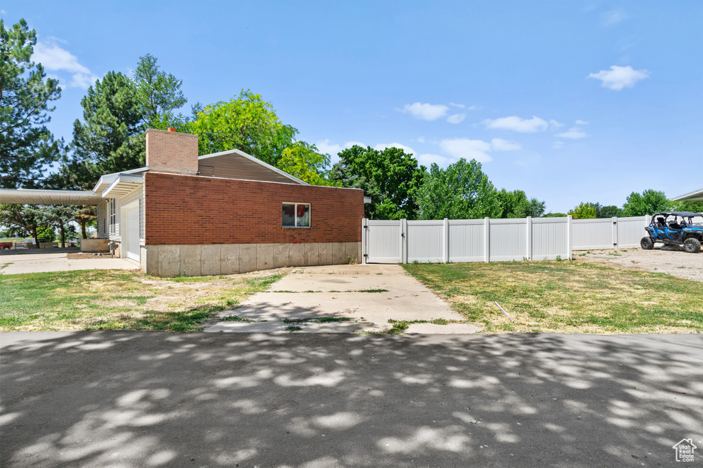 View of side of property featuring a gate, a chimney, an attached garage, and driveway