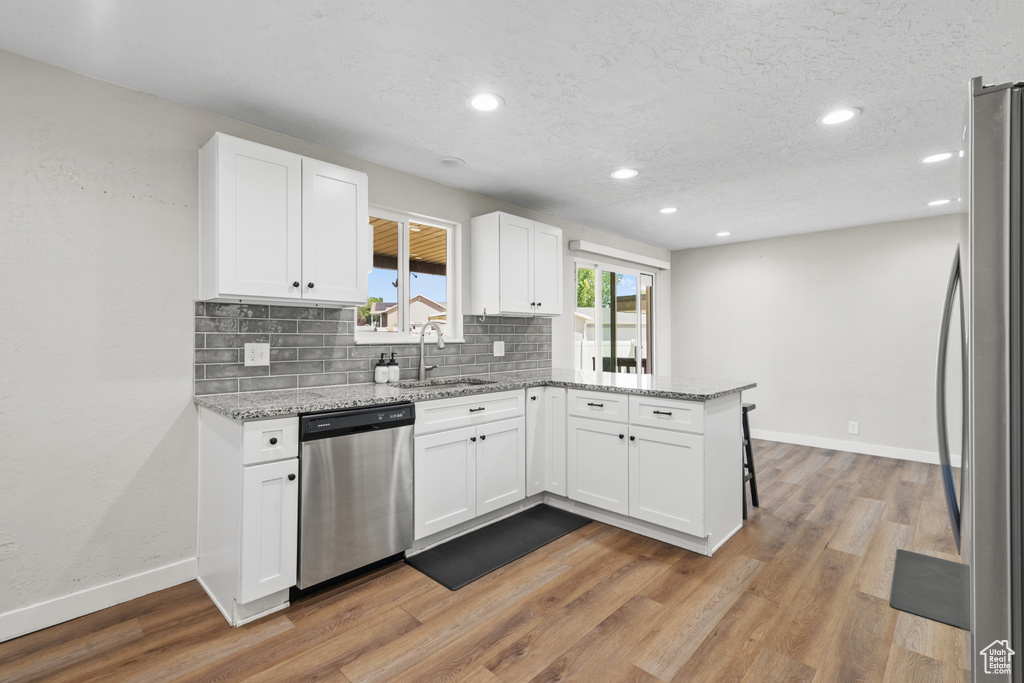 Kitchen featuring stainless steel appliances, a peninsula, white cabinets, tasteful backsplash, and light stone counters