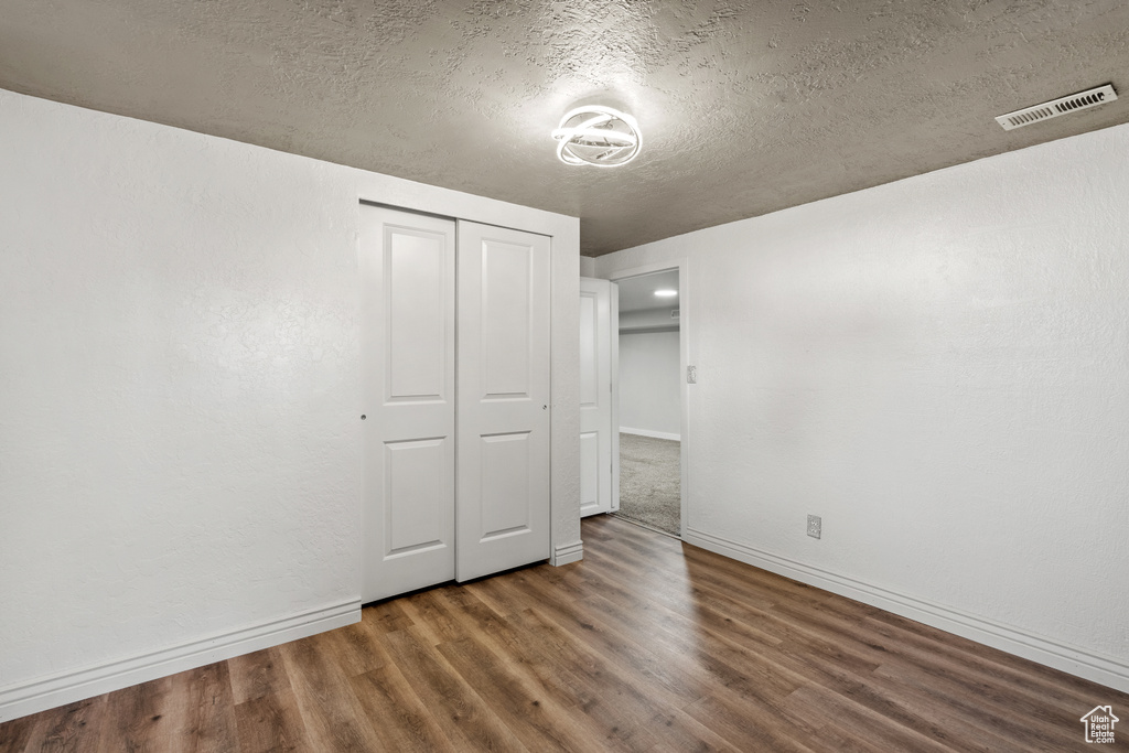 Unfurnished bedroom with a textured ceiling, wood finished floors, and a closet