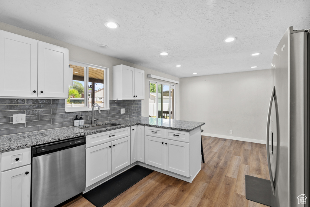 Kitchen with stainless steel appliances, a peninsula, decorative backsplash, light stone countertops, and white cabinets