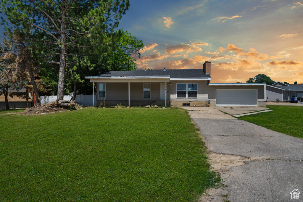 Ranch-style home featuring a front lawn, a chimney, concrete driveway, and a garage