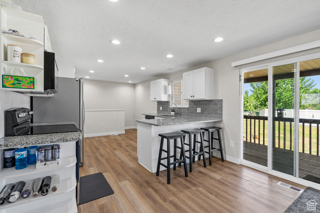 Kitchen with a breakfast bar area, white cabinets, open shelves, light wood-style flooring, and tasteful backsplash