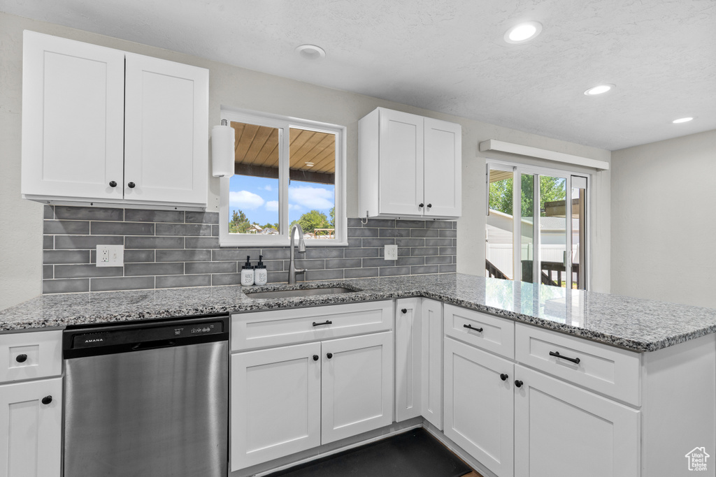 Kitchen featuring dishwasher, a peninsula, white cabinetry, tasteful backsplash, and light stone counters