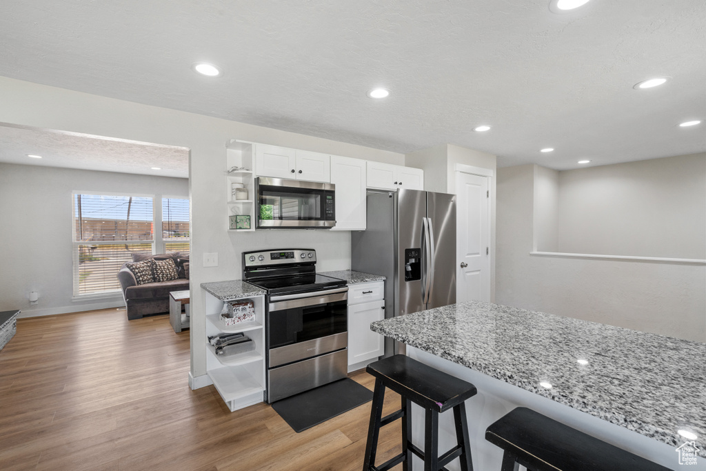 Kitchen with appliances with stainless steel finishes, light wood-style floors, white cabinets, a breakfast bar area, and light stone counters