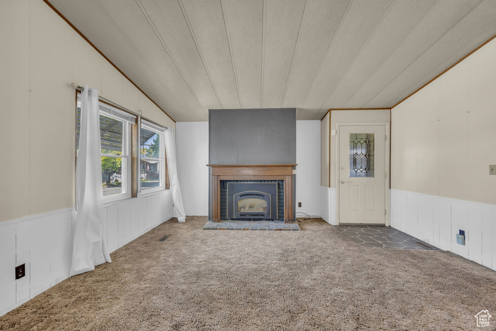 Unfurnished living room featuring carpet flooring, vaulted ceiling, a brick fireplace, a wainscoted wall, and a decorative wall