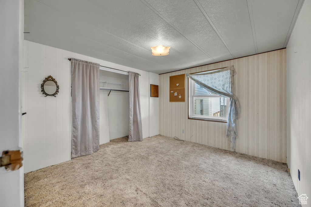 Unfurnished bedroom featuring a closet, carpet flooring, a textured ceiling, and wooden walls
