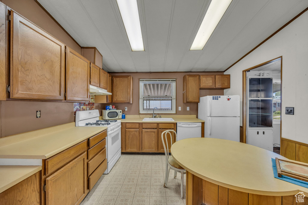 Kitchen featuring white appliances, under cabinet range hood, light countertops, light floors, and brown cabinetry