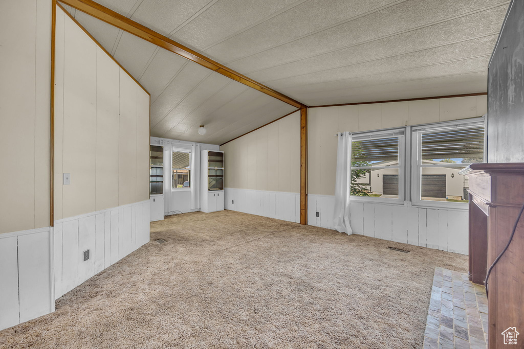 Carpeted empty room with lofted ceiling, a decorative wall, and wainscoting