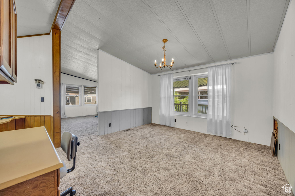 Dining room with plenty of natural light, a chandelier, carpet flooring, vaulted ceiling, and wooden walls