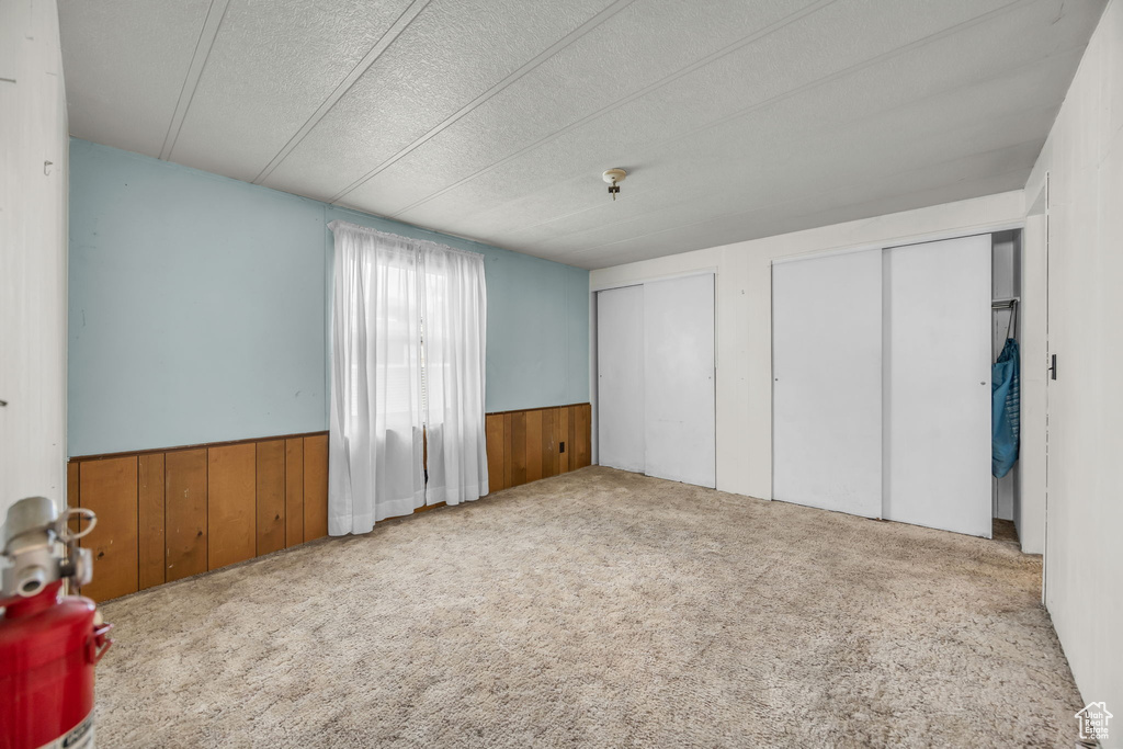 Unfurnished bedroom featuring two closets, wooden walls, a wainscoted wall, carpet flooring, and a textured ceiling