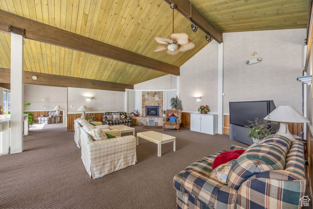 Carpeted living area featuring a wooden ceiling with exposed beams, a ceiling fan, wainscoting, a fireplace, and high vaulted ceiling