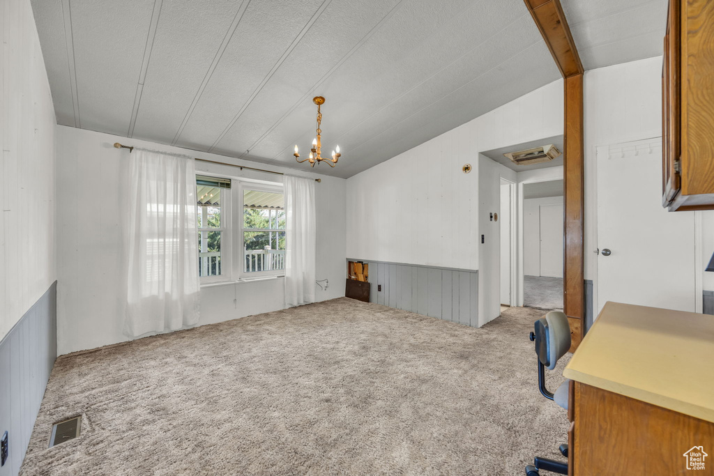 Unfurnished living room featuring lofted ceiling, carpet floors, a chandelier, and wainscoting