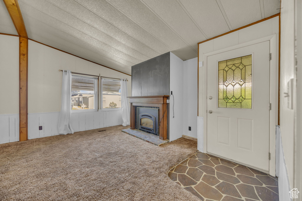 Unfurnished living room with vaulted ceiling, a fireplace with raised hearth, and carpet flooring