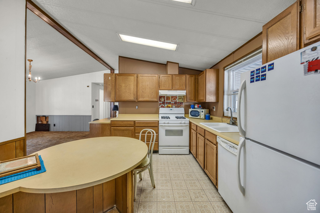 Kitchen with white appliances, under cabinet range hood, vaulted ceiling, wainscoting, and light countertops