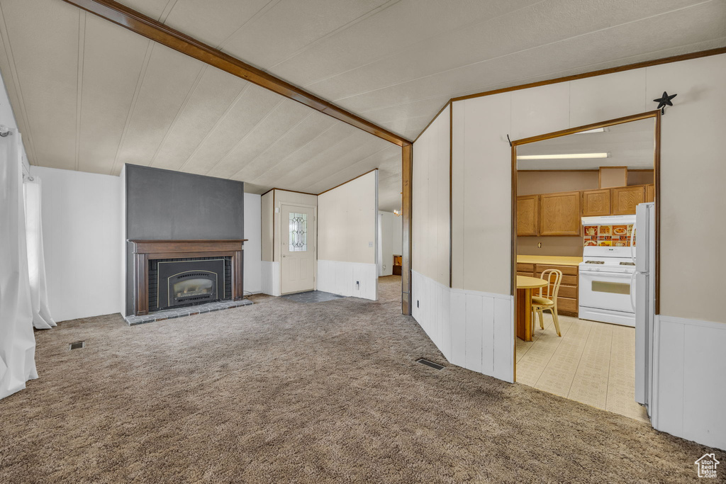 Unfurnished living room featuring light carpet, vaulted ceiling, wainscoting, and a brick fireplace