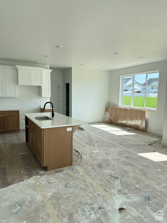 Kitchen with a textured ceiling, open floor plan, an island with sink, white cabinetry, and light countertops