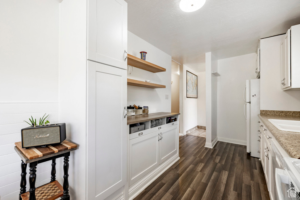 Kitchen featuring freestanding refrigerator, dark wood-style floors, open shelves, white cabinets, and light countertops