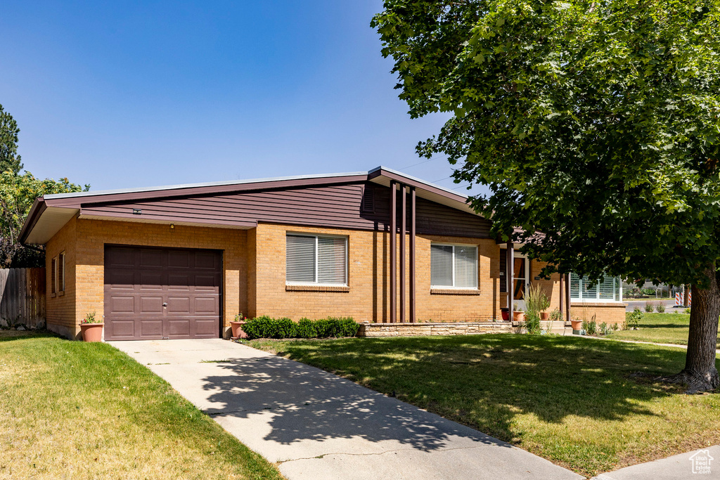 View of front of house with brick siding, driveway, a front lawn, and a garage