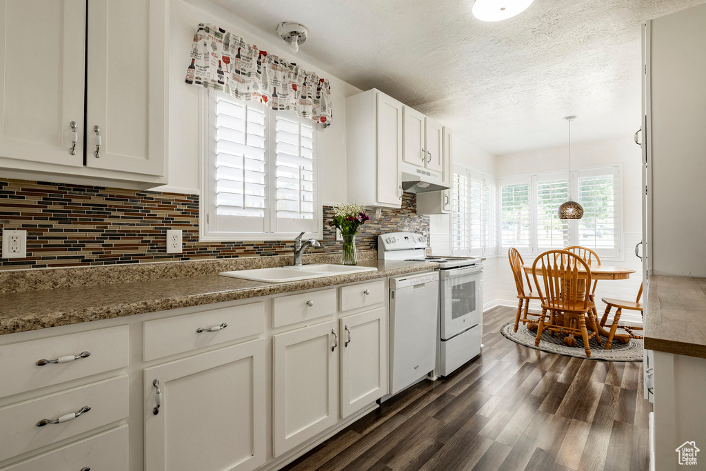 Kitchen featuring white appliances, under cabinet range hood, decorative backsplash, dark wood-style flooring, and white cabinets