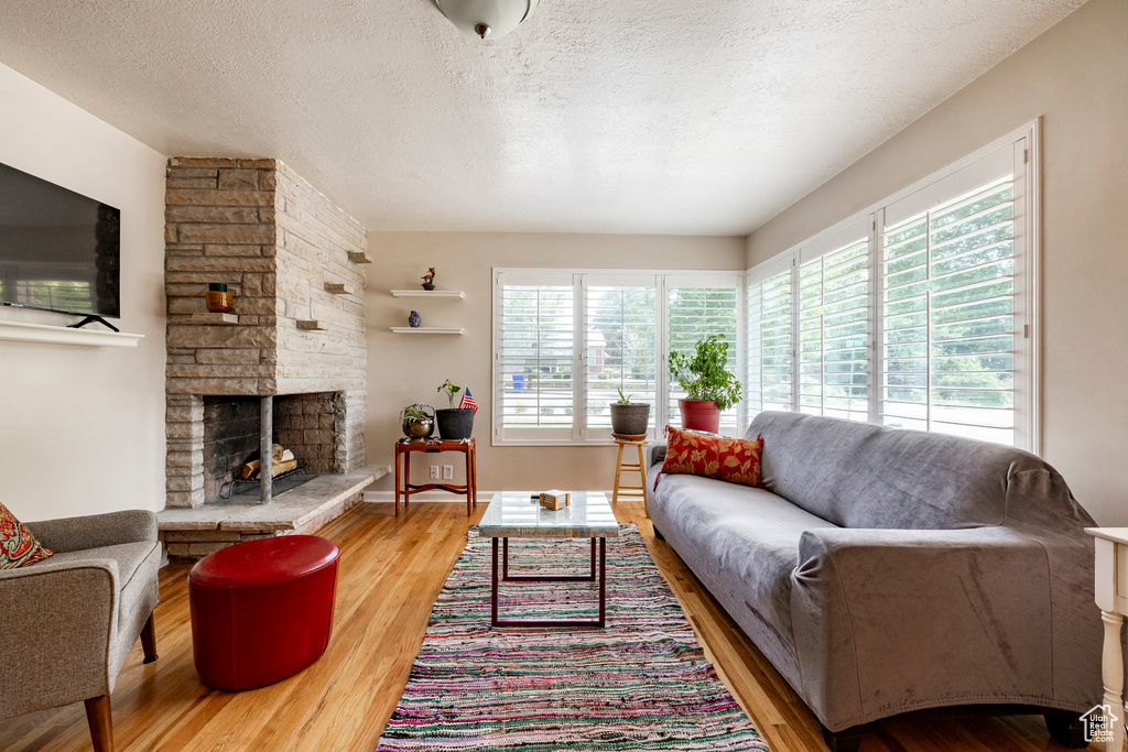 Living area featuring healthy amount of natural light, wood finished floors, a textured ceiling, and a stone fireplace