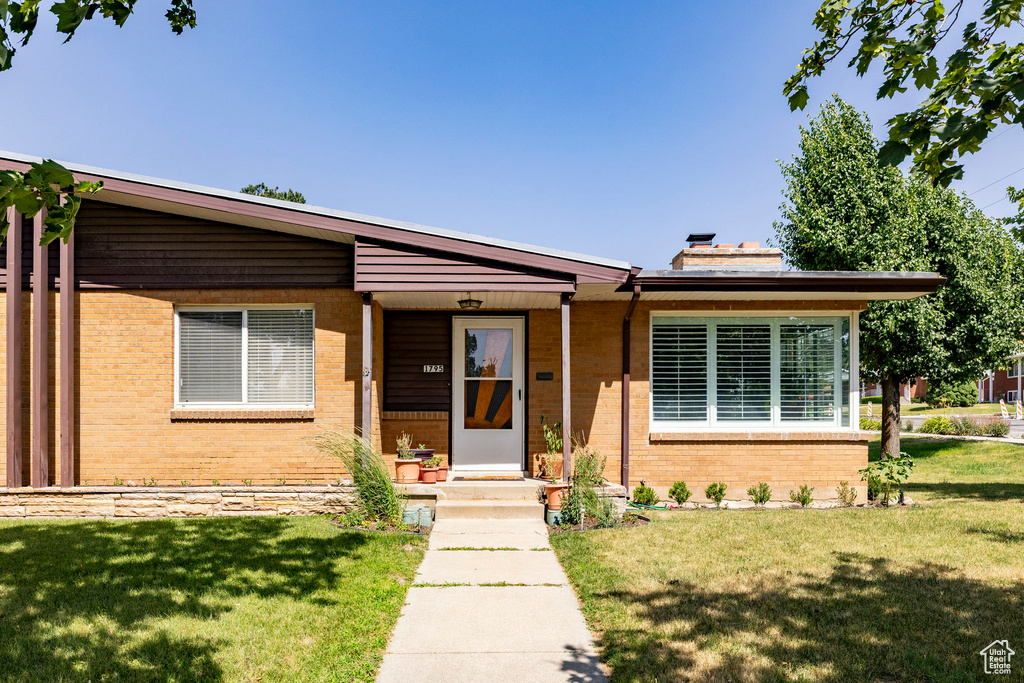 View of front of house with brick siding, a front lawn, and a chimney