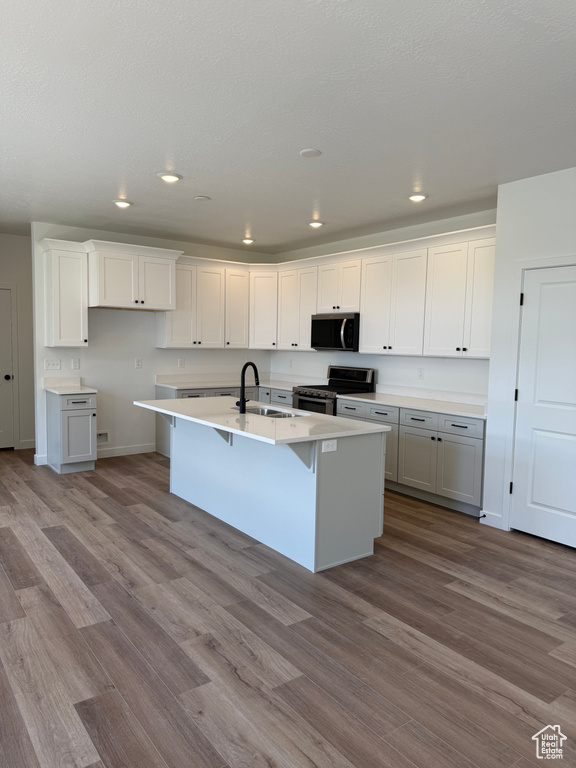 Kitchen featuring electric range, wood finished floors, an island with sink, recessed lighting, and a kitchen breakfast bar