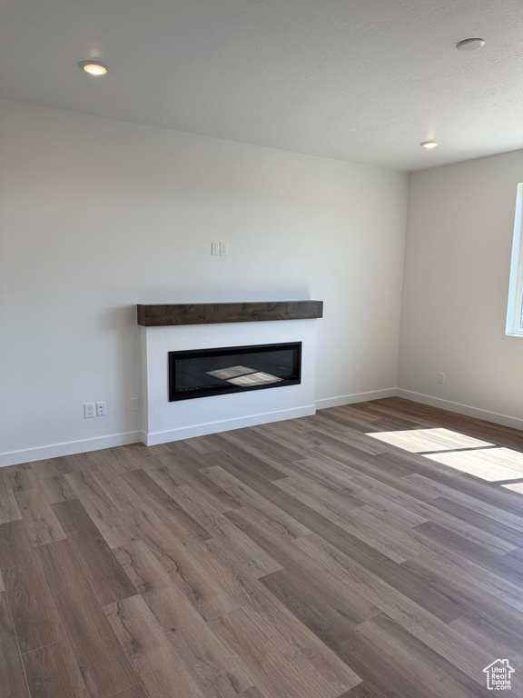 Unfurnished living room featuring a glass covered fireplace, wood finished floors, and recessed lighting