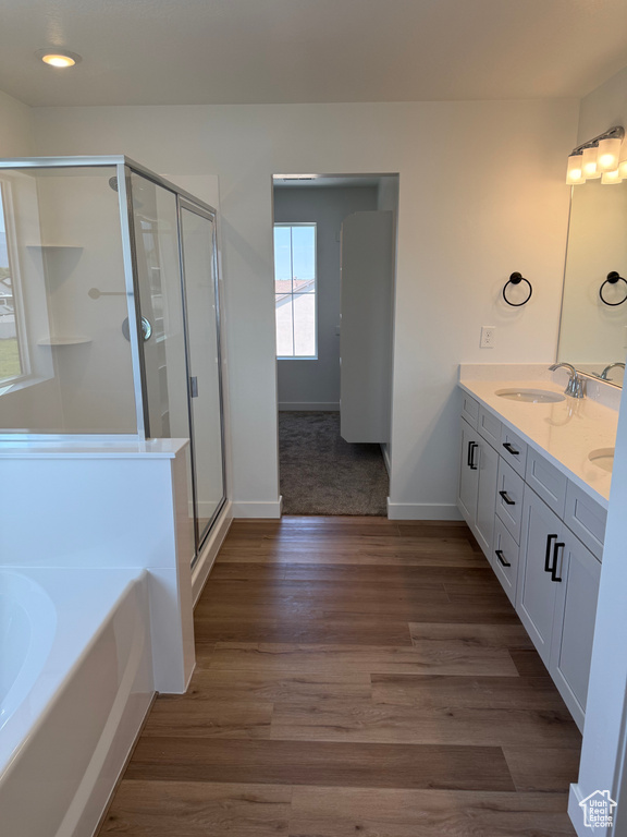 Full bathroom with double vanity, a garden tub, a stall shower, wood finished floors, and recessed lighting