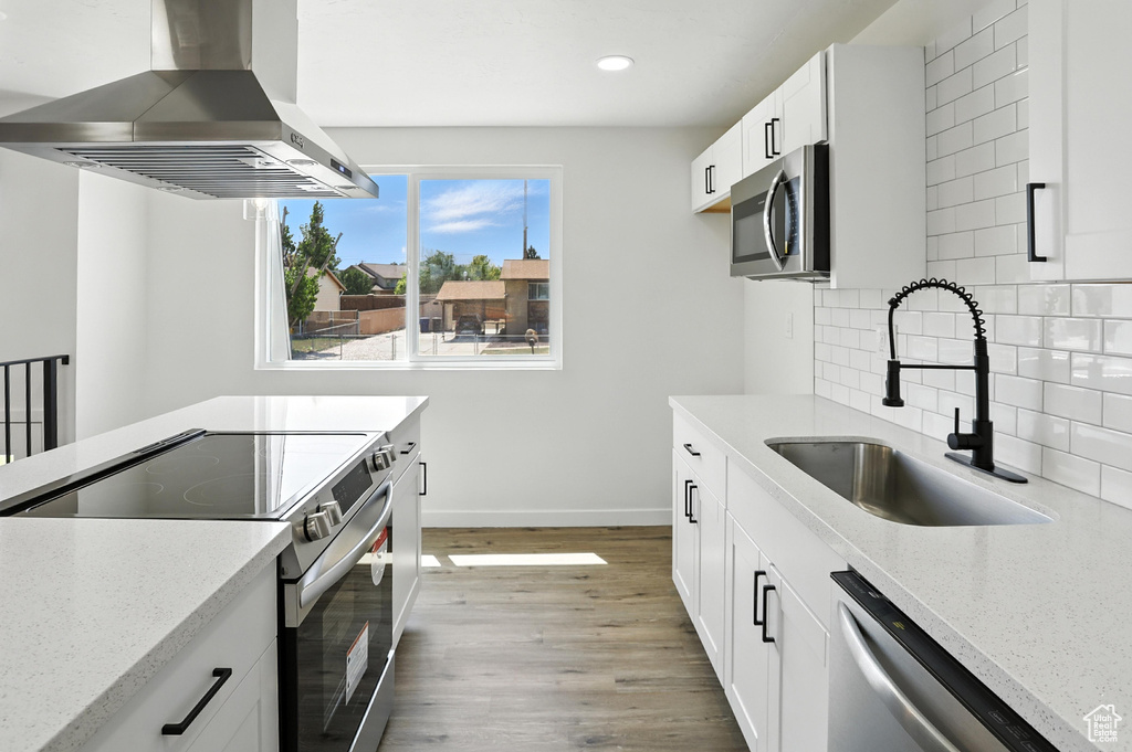 Kitchen with island range hood, stainless steel appliances, light stone counters, light wood-style floors, and decorative backsplash