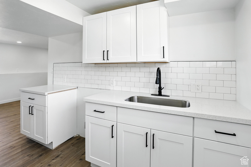 Kitchen featuring dark wood-style flooring, decorative backsplash, white cabinets, and light stone counters