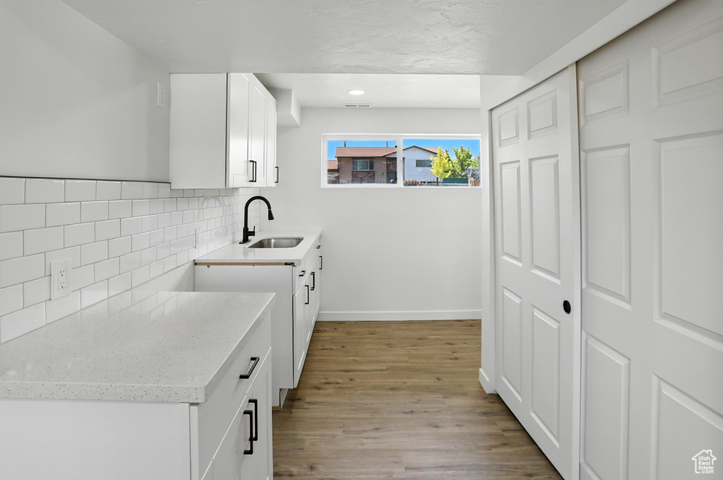 Kitchen with backsplash, light wood-style flooring, light stone countertops, white cabinetry, and recessed lighting