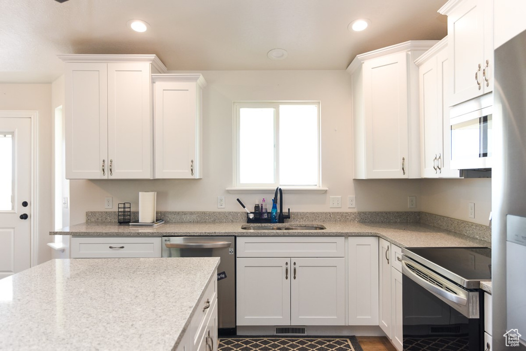 Kitchen with stainless steel appliances, white cabinetry, recessed lighting, and light stone countertops