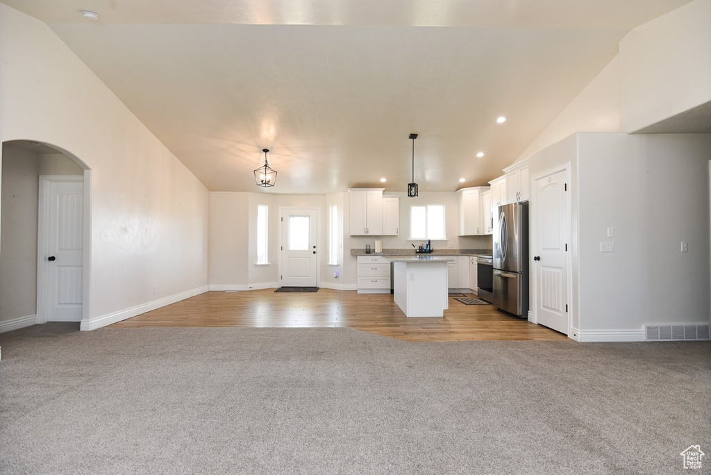 Kitchen with freestanding refrigerator, light colored carpet, open floor plan, lofted ceiling, and white cabinets