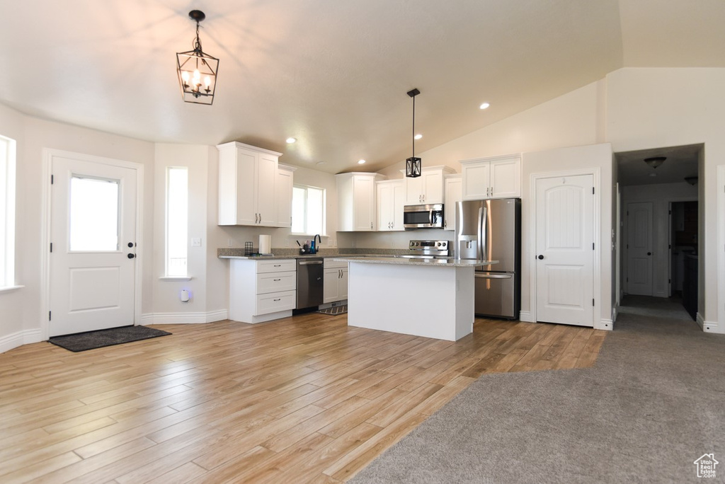 Kitchen with stainless steel appliances, lofted ceiling, a kitchen island, white cabinets, and light wood-style floors