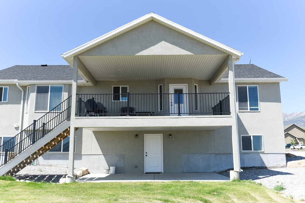 Rear view of house with stucco siding, stairway, a patio, and a shingled roof