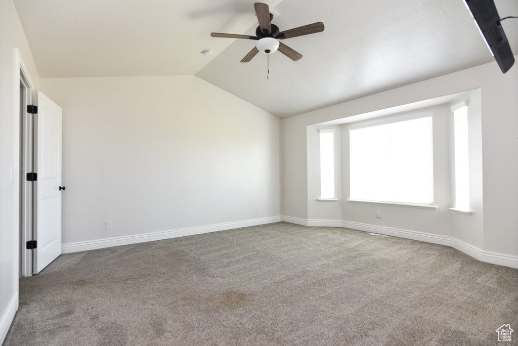 Carpeted empty room featuring a ceiling fan and lofted ceiling