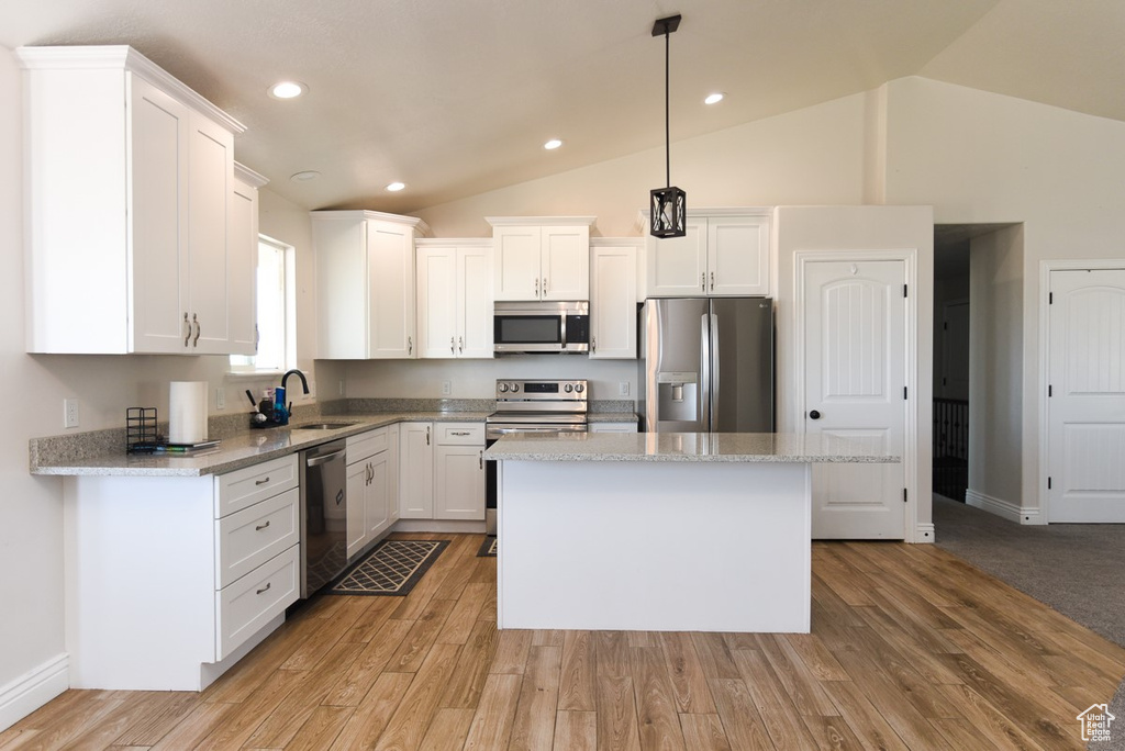 Kitchen featuring stainless steel appliances, a kitchen island, white cabinets, decorative light fixtures, and light wood-style flooring