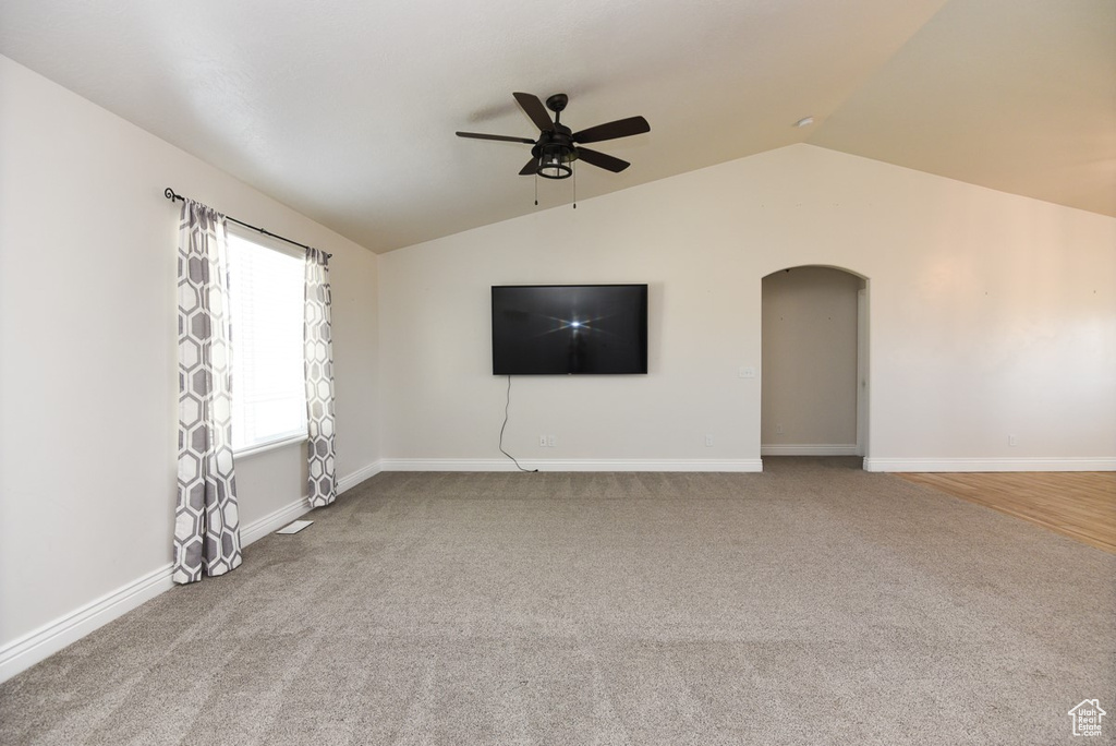 Unfurnished living room with lofted ceiling, ceiling fan, arched walkways, and carpet flooring