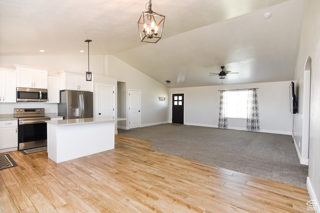 Kitchen featuring stainless steel appliances, a kitchen island, white cabinetry, open floor plan, and hanging light fixtures