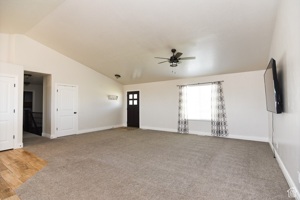 Unfurnished living room featuring a ceiling fan, vaulted ceiling, and carpet