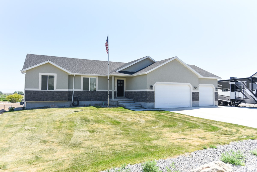 Ranch-style home with an attached garage, stucco siding, driveway, stone siding, and a front yard