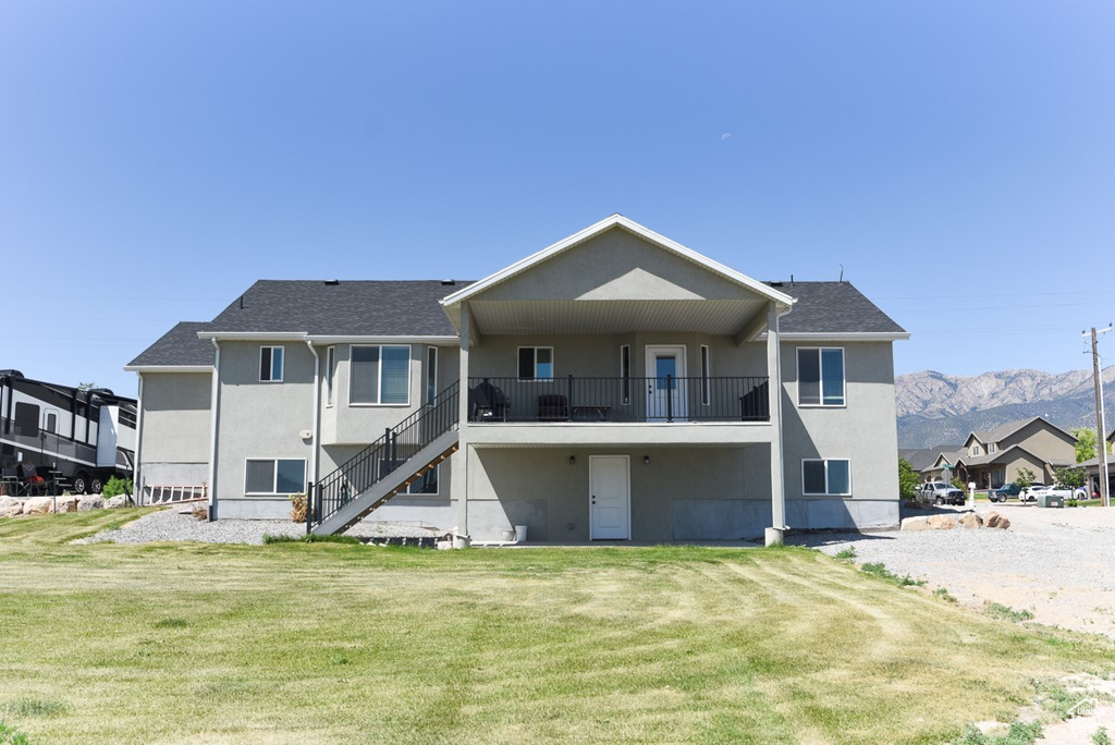 Rear view of property featuring stucco siding, stairway, a lawn, a mountain view, and a shingled roof
