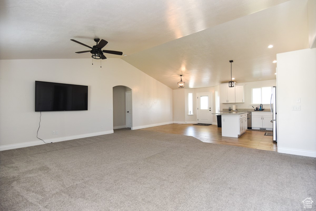 Unfurnished living room with light colored carpet, a ceiling fan, arched walkways, and lofted ceiling
