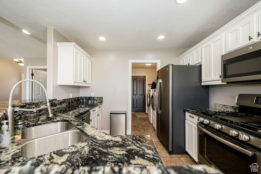 Kitchen featuring appliances with stainless steel finishes, washing machine and clothes dryer, white cabinetry, dark stone counters, and recessed lighting