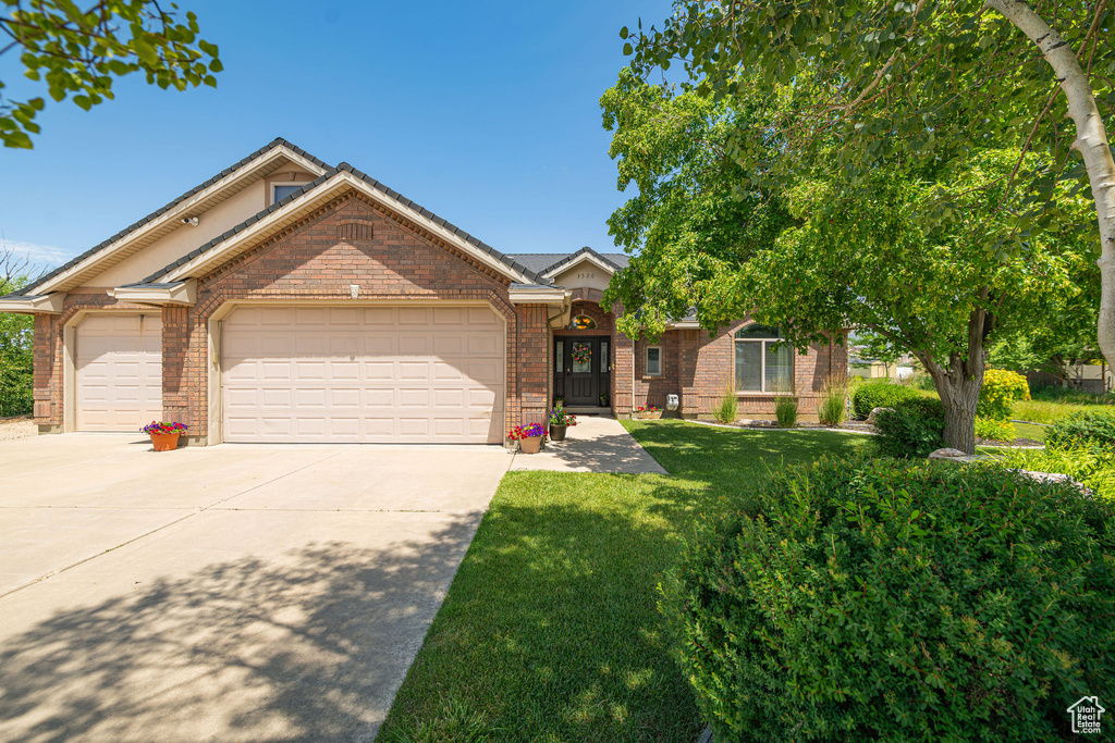 View of front of home with brick siding, driveway, an attached garage, and a front lawn