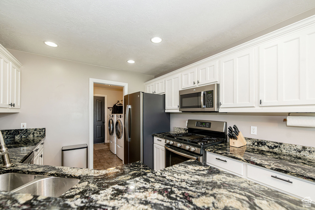 Kitchen featuring appliances with stainless steel finishes, washer and dryer, white cabinets, dark stone counters, and recessed lighting