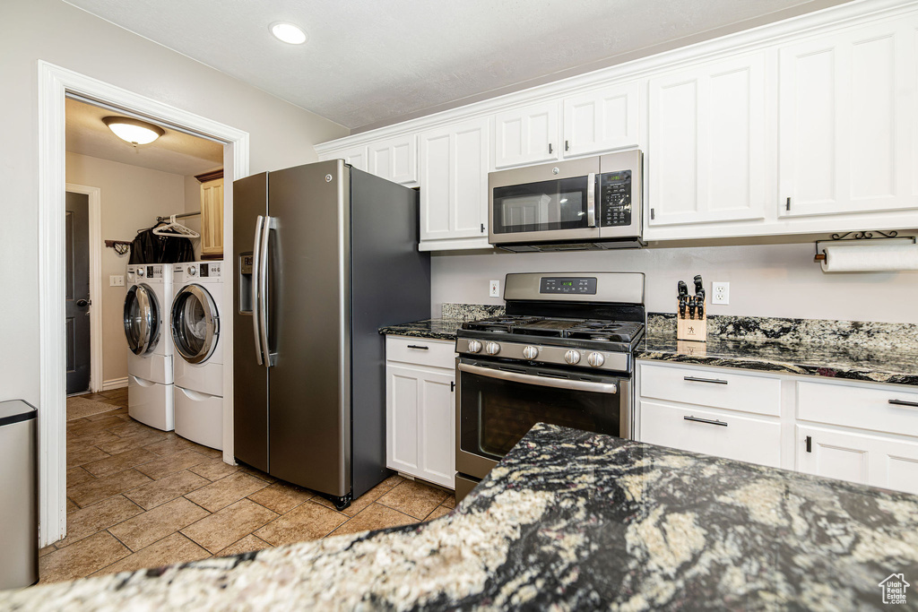 Kitchen featuring stainless steel appliances, washer and dryer, white cabinetry, dark stone countertops, and recessed lighting