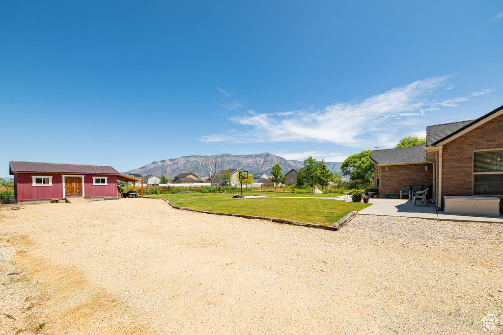 View of green lawn with a mountain view, a patio, and driveway